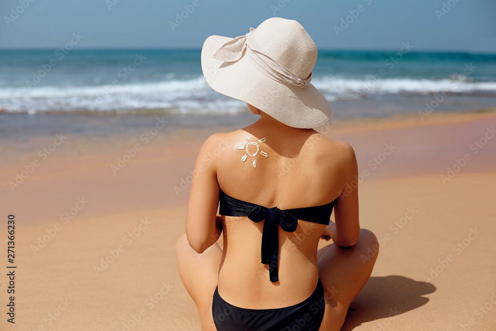 Young woman with sun shape on the shoulder holding sun cream bottle on the beach Young woman with sun shape on the shoulder holding sun cream bottle on the beach