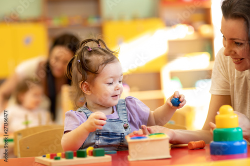 Babies with teachers playing with developmental toys in nursery photo