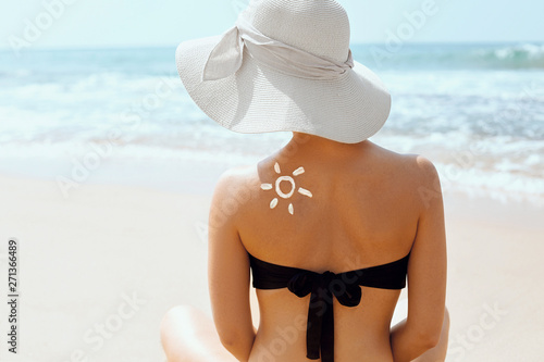 Beautiful woman in bikini applying sun cream on tanned shoulder. Sun protection. Skin and body care. Girl using sunscreen to skin. Portrait of female holding suntan lotion and moisturizing sunblock.
