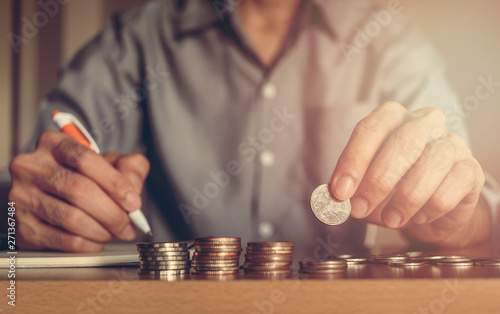 Businessman puts a coins to stack of coins and record for accounting, save money, business concept.