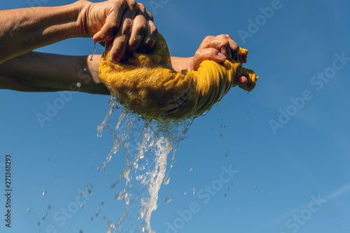 Hands squeeze yellow cloth outdoors.