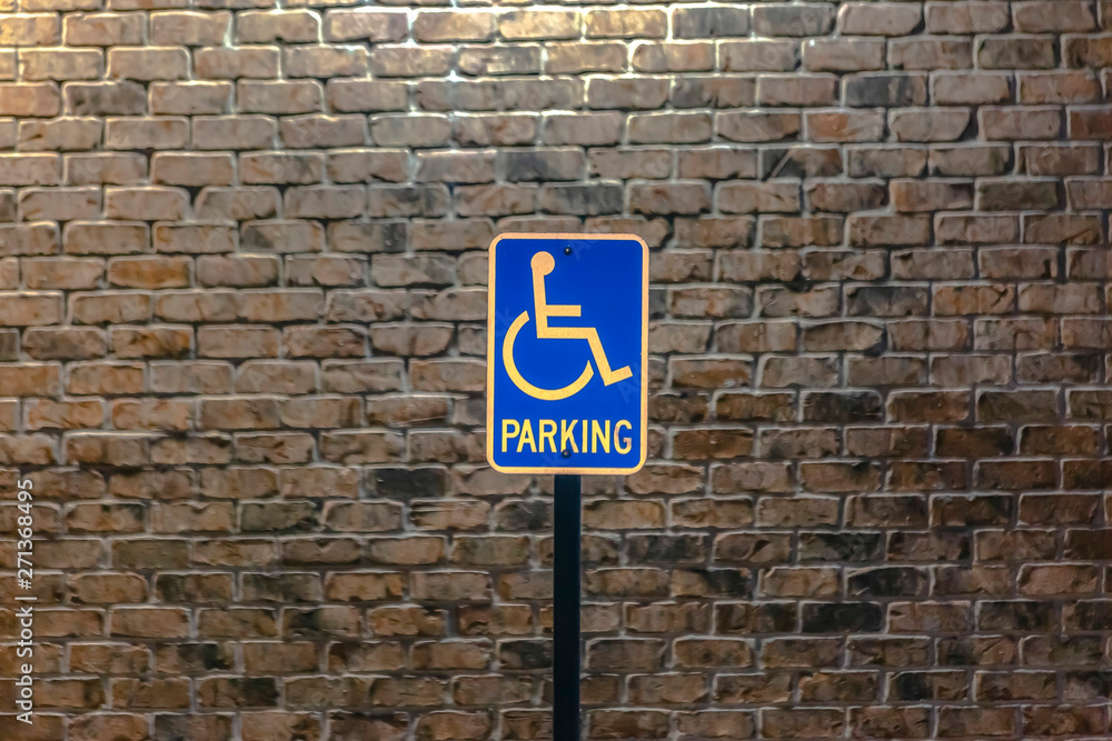 Handicap parking sign against a stone brick wall illuminated by sunlight Handicap parking sign against a stone brick wall illuminated by sunlight