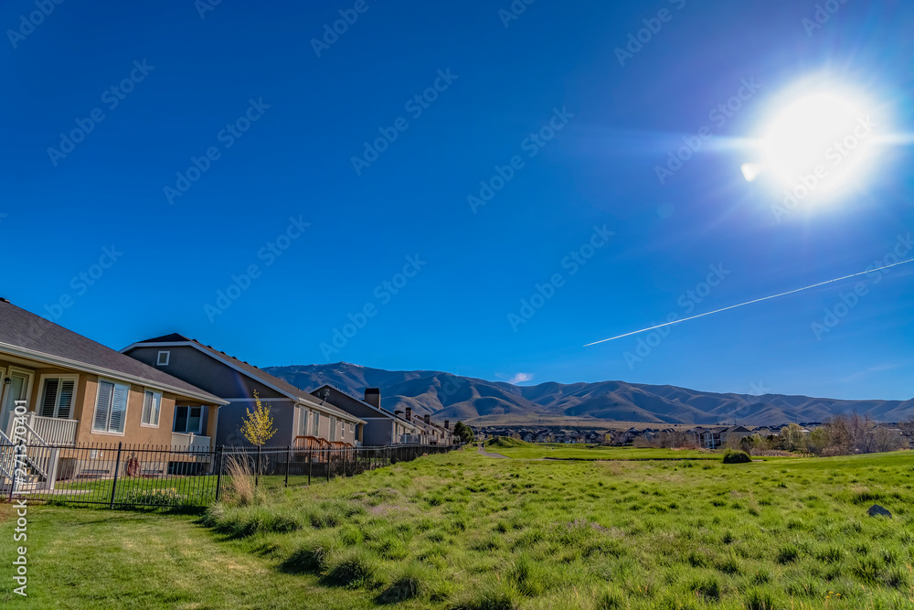 Houses on a lush grassy field under the blazing sun and vivid blue sky Houses on a lush grassy field under the blazing sun and vivid blue sky