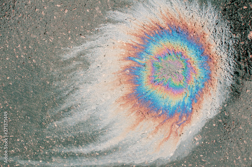 Colorful rainbow spot on black asphalt from spilled engine oil