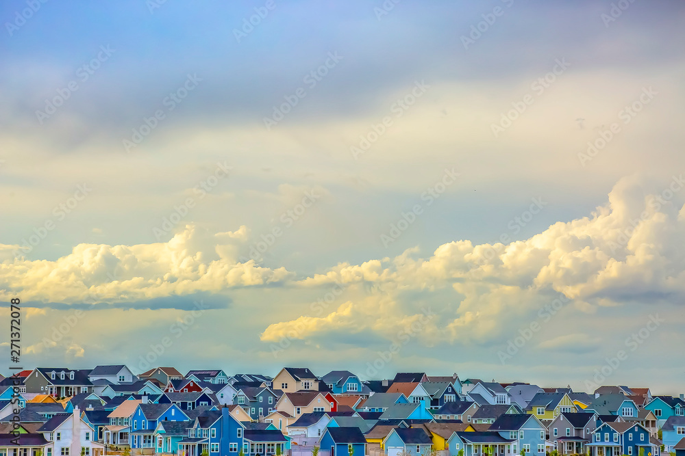 Panoramic view of houses under vast sky filled with illuminated puffy clouds