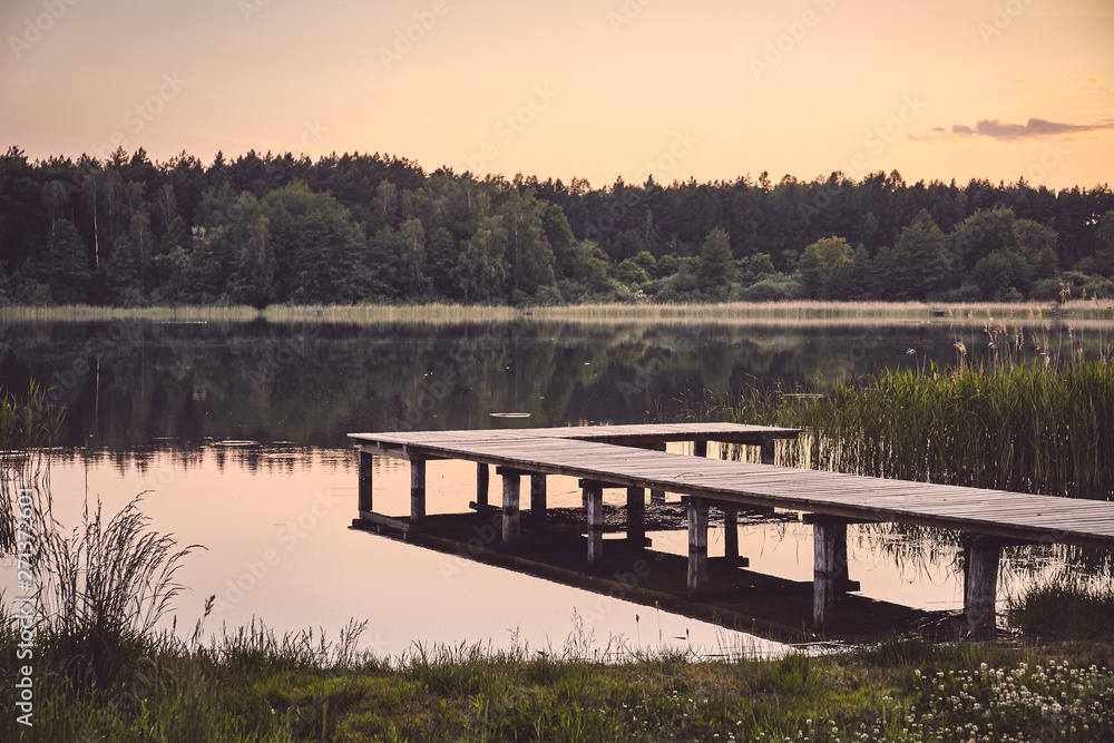 Wooden pier at a calm lake at sunset, color toning applied.