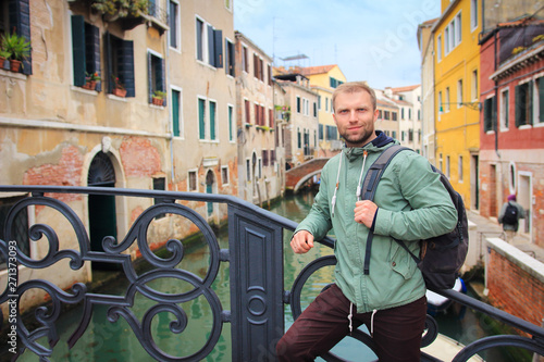 Obraz na płótnie Tourist man in Venice, Italy. Portrait of handsome young guy with backpack against venetian water canal w salonie
