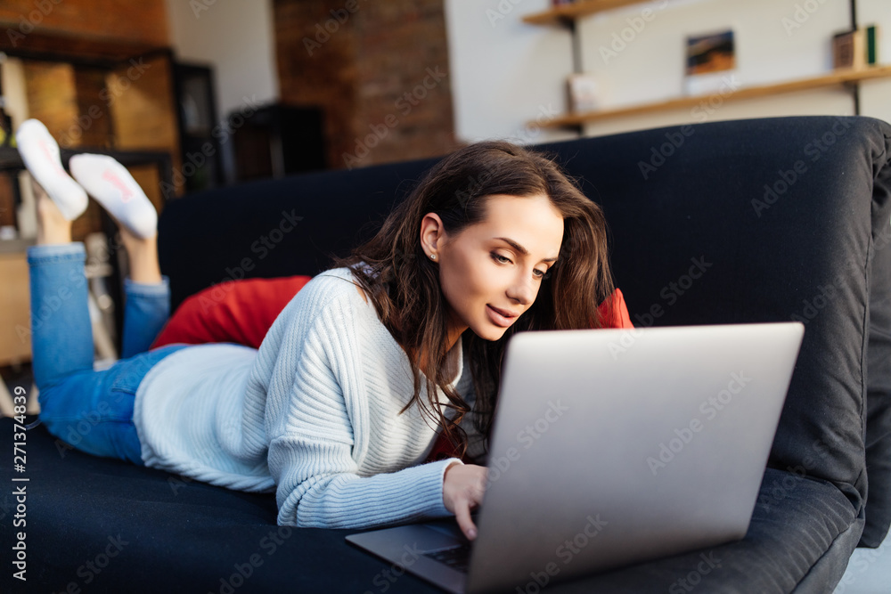 Young woman lying on couch with laptop at home Young woman lying on couch with laptop at home