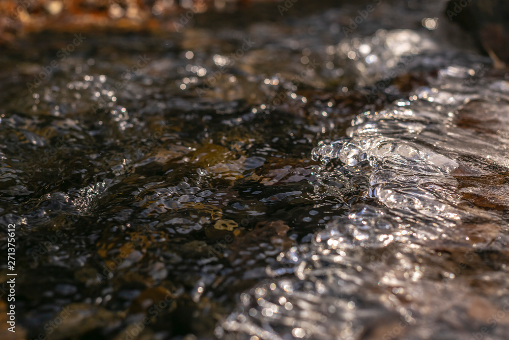 Close up of a stream with translucent frozen water over dark rocks Close up of a stream with translucent frozen water over dark rocks