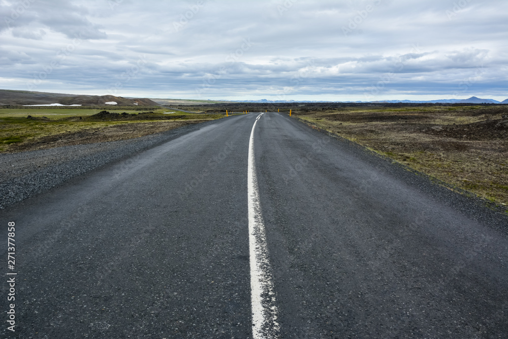 View to the empty curvy road, empty meadow and red mountains in the background in Myvatn region, overcast day in summer View to the empty curvy road, empty meadow and red mountains in the background in Myvatn region, overcast day in summer