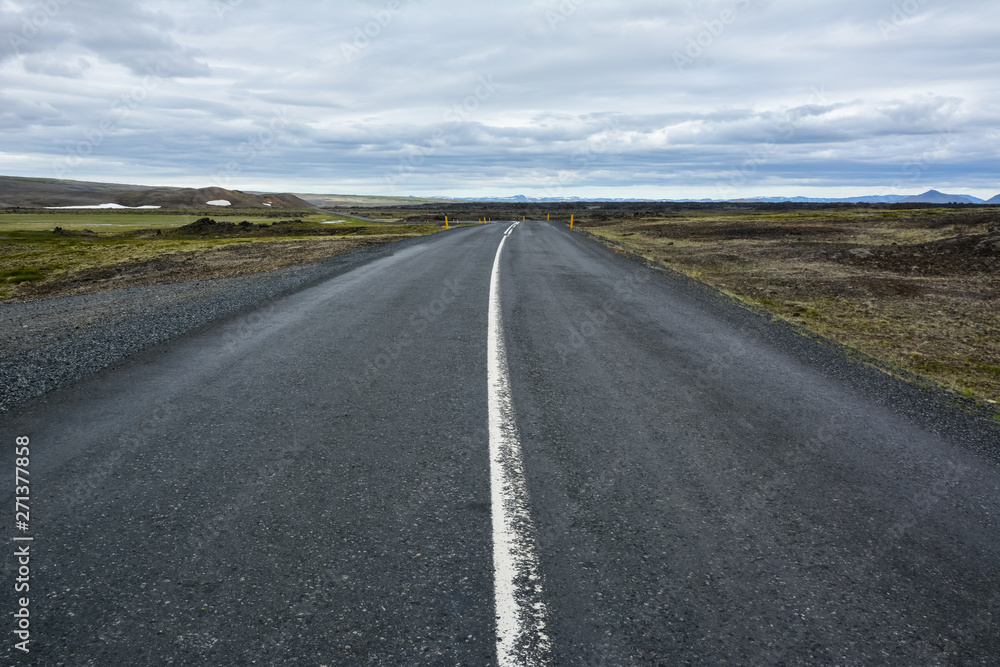 View to the empty curvy road, empty meadow and red mountains in the background in Myvatn region, overcast day in summer