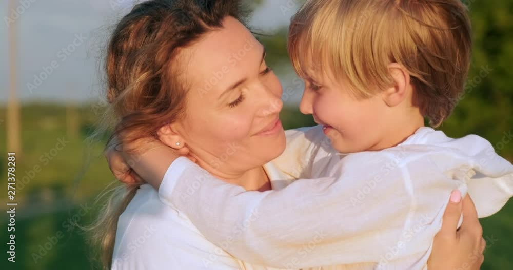 Happy mother kissing her son on hands walking on the meadow in summer. Mother with 7 year child strolls on field. Adult mother with blond boy sauntering in nature. Slow motion. Happiness. Happy mother kissing her son on hands walking on the meadow in summer. Mother with 7 year child strolls on field. Adult mother with blond boy sauntering in nature. Slow motion. Happiness.