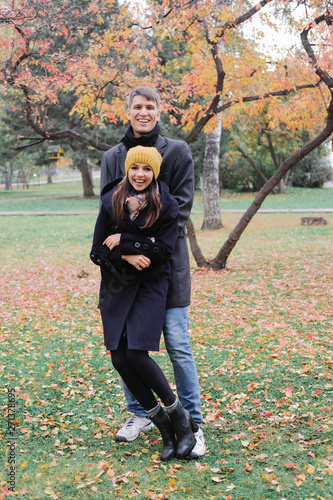 Smiling lovers hold hands and look at each other. A man and a woman in a black coat on background of autumn park.