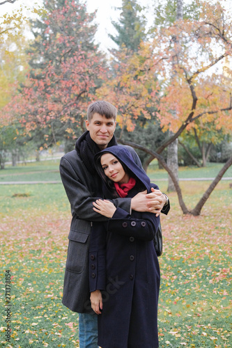Smiling lovers hold hands and look at each other. A man and a woman in a black coat on background of autumn park.