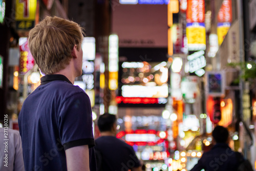 A young tourist looking off to the distance in a neon lit Tokyo street