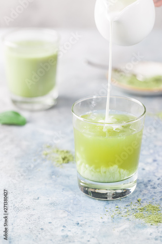 Iced Matcha green latte in glasses with matcha powder on light background.