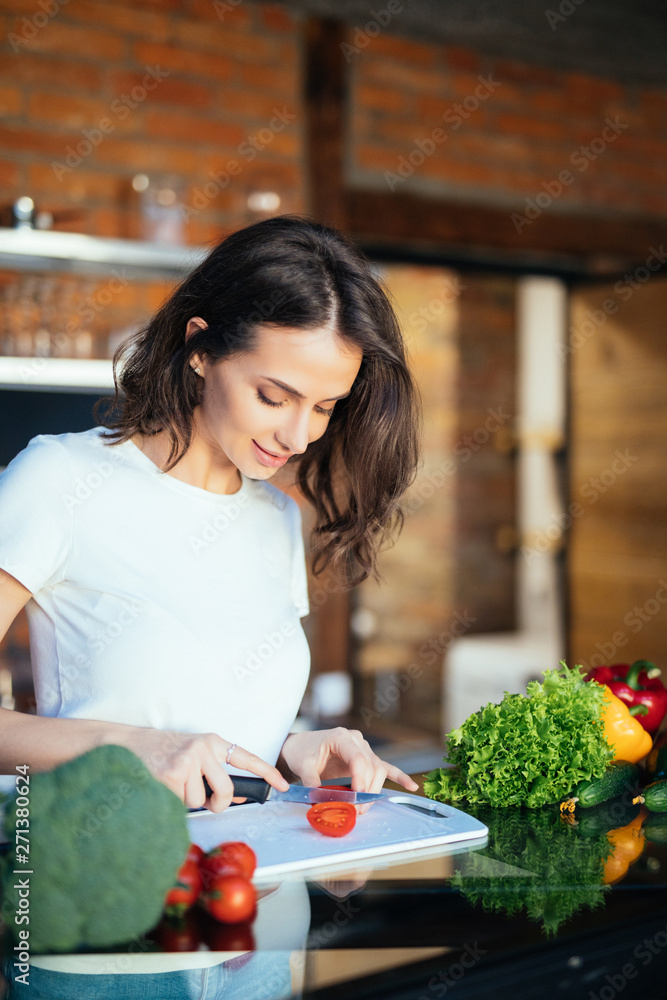 Portrait of beautiful woman slice, cutting tomato in the kitchen, cooking, prepare vegetable salad