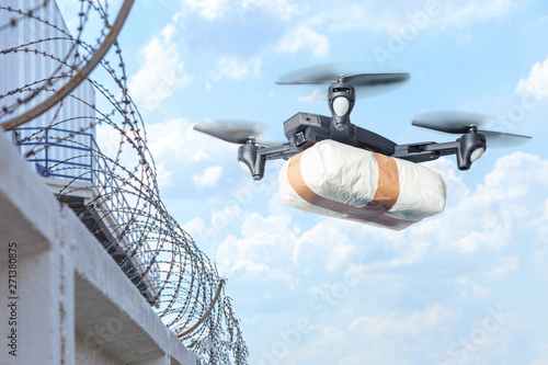 The drone flew across the sky with smuggling. The drone transports forbidden goods across the border breaking the law. Delivery of drugs through the wall with barbed wire photo