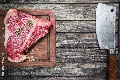 Raw T-bone Steak with fresh herbs and oil on dark wooden background, top view