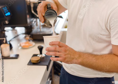 Young barista pouring and serving to go paper cup of coffee