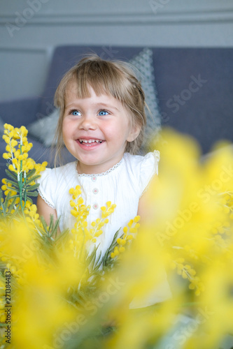 A cute little girl with light brown hair sniffs a bouquet of fragrant yellow mimosa, donated on March 8 on International Women's Day.