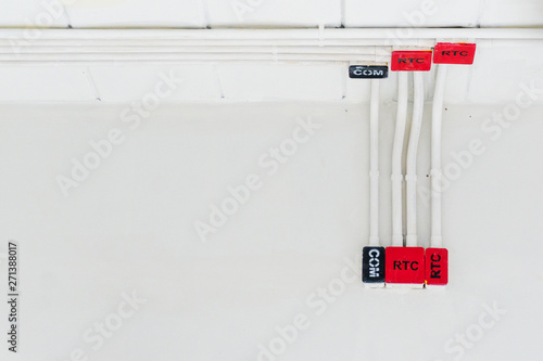 White electric PVC pipe in red and black are connected to power lines or electrical wires, Ethernet UTP cables, internet and light boxes on building wall. Concept for construction and system building.