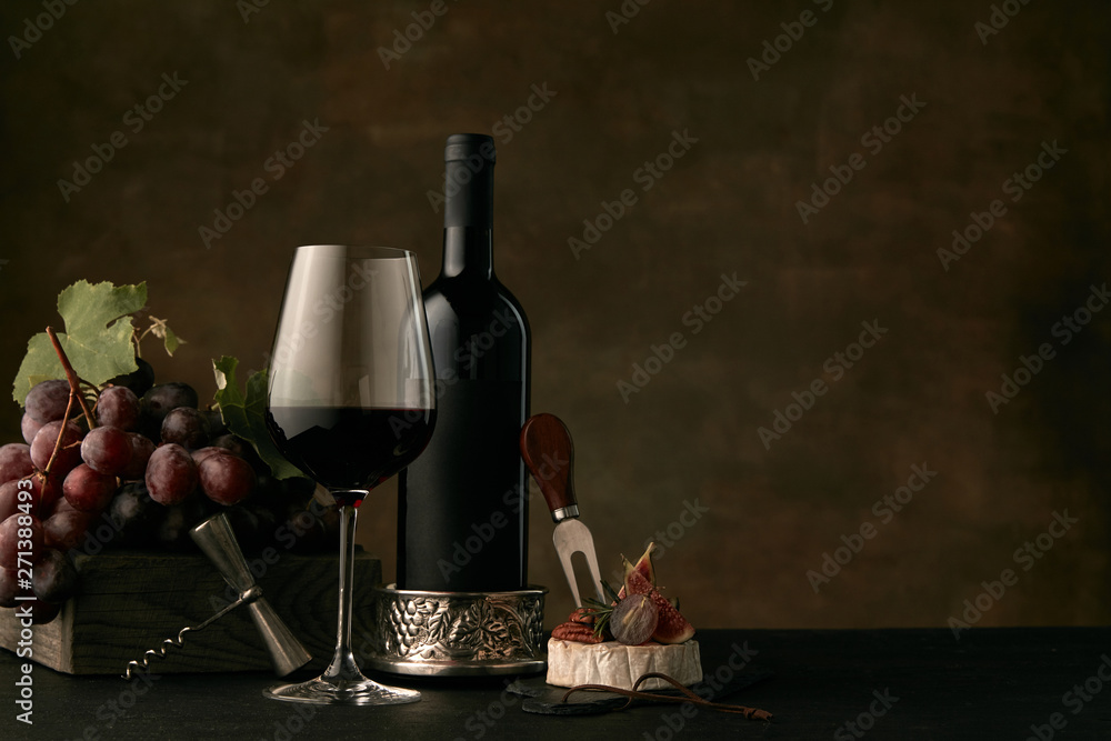 Front view of tasty fruit plate of grapes with the wine bottle, cheese and wineglass on dark studio background, copy space to insert your text or image. Gourmet food and drink.