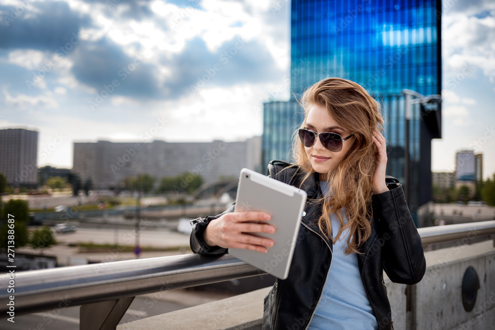 Young smiling woman using tablet among modern office buildings on city street