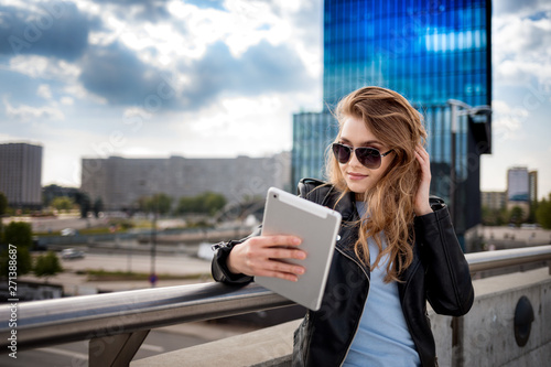 Young smiling woman using tablet among modern office buildings on city street photo
