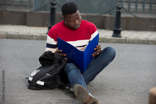 Handsome college man reading notes in notebook on campus.