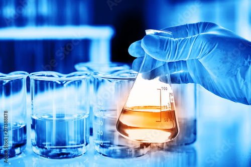 Flask in scientist hand with lab glassware background in laboratory. Science or chemical research and development concept.  photo