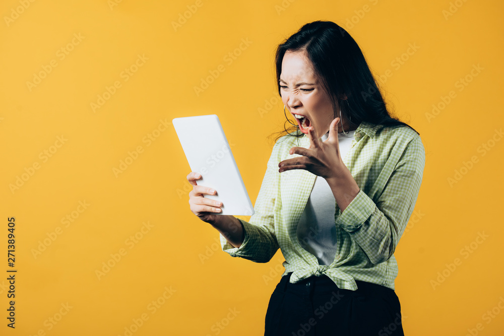 angry asian girl shouting and using digital tablet, isolated on yellow