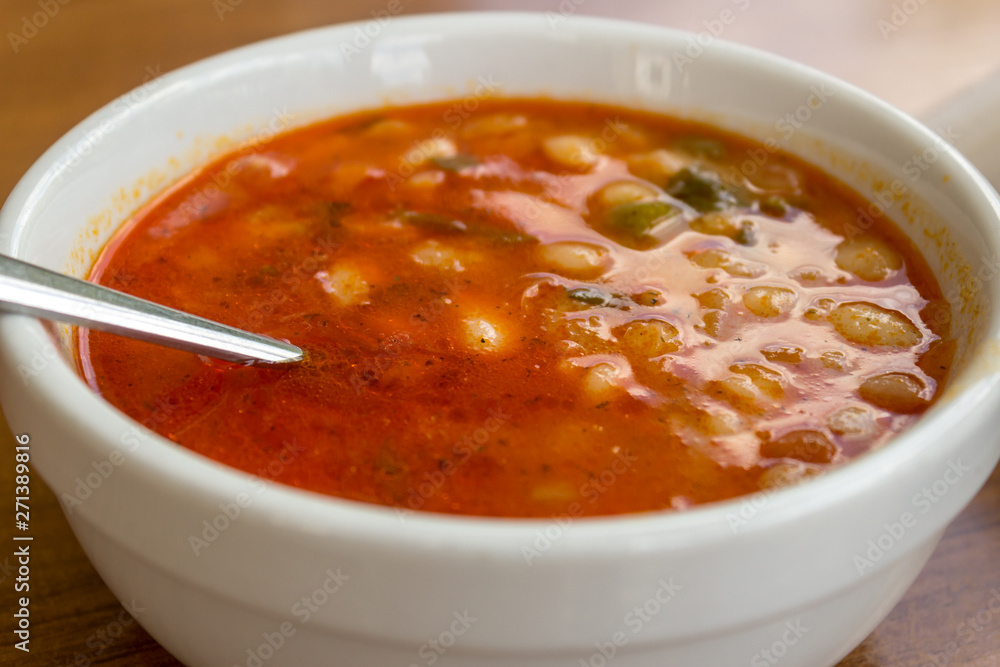 White beans in tomato sauce in a bowl with a spoon in on wooden table at a restaurant. White beans in tomato sauce in a bowl with a spoon in on wooden table at a restaurant.