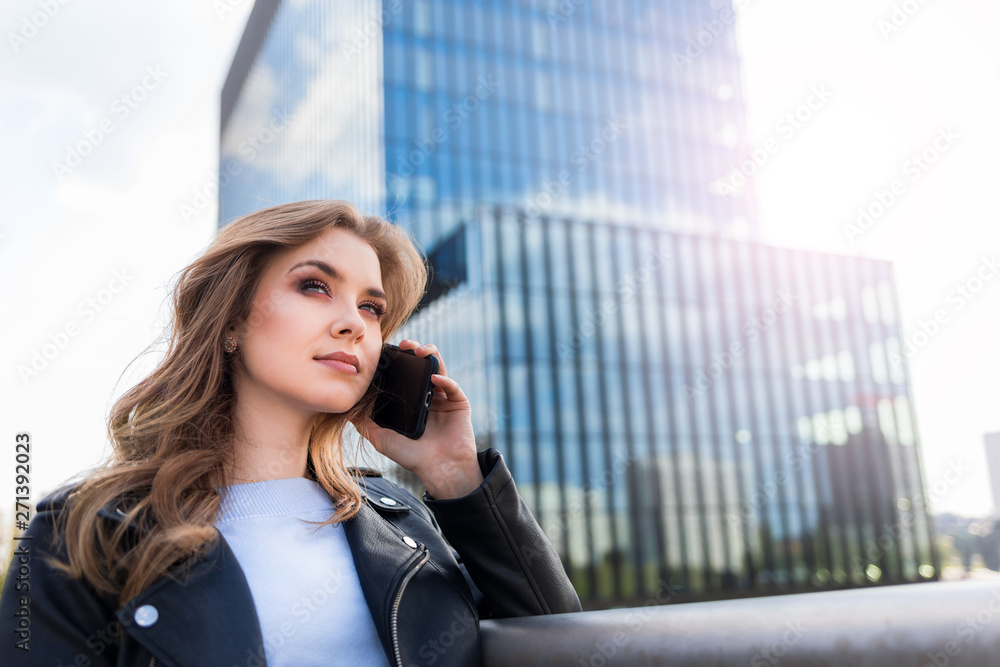 Successfull young businesswoman talking on phone with modern office buildings in the background Successfull young businesswoman talking on phone with modern office buildings in the background