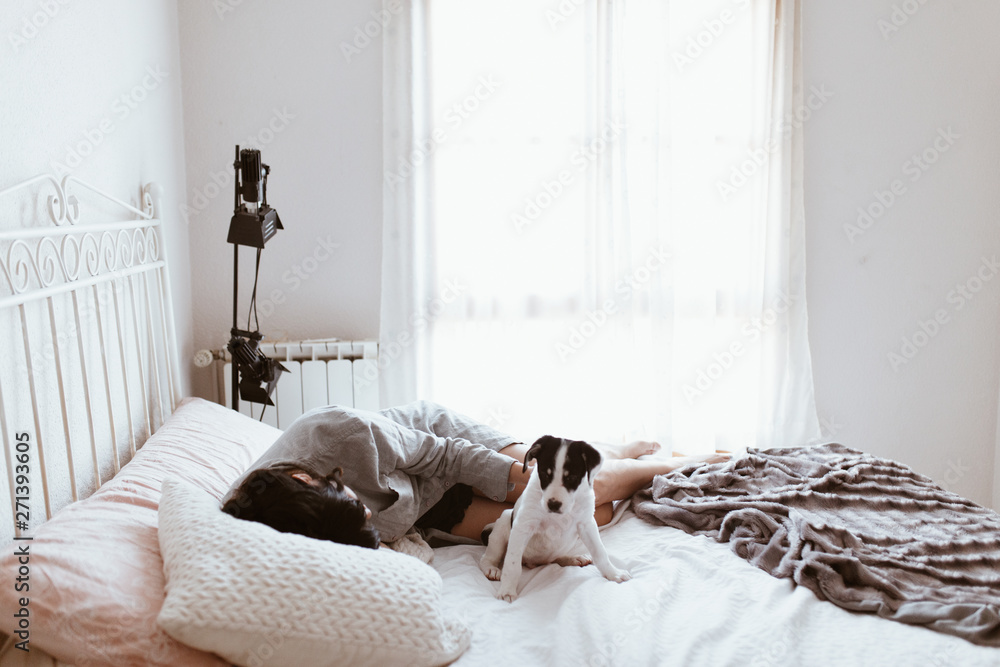 Young sad brunette woman caressing her labrador puppy lying in bedroom Young sad brunette woman caressing her labrador puppy lying in bedroom
