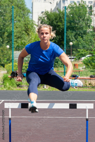 A beautiful and athletic girl is running hurdles in the stadium