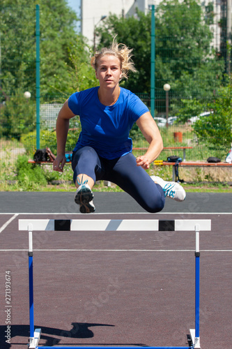 A beautiful and athletic girl is running hurdles in the stadium