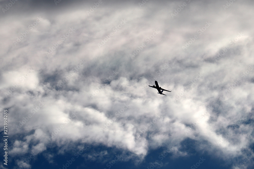 Airplane flying in the sky on background of clouds. Silhouette of a commercial plane during the turn