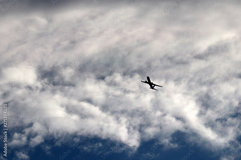 Airplane flying in the sky on background of clouds. Silhouette of a commercial plane during the turn Airplane flying in the sky on background of clouds. Silhouette of a commercial plane during the turn