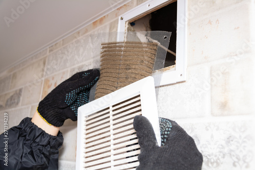 repair service man removing a dirty air filter on a house so he can replace it with a new clean. Extremely dirty and dusty white plastic ventilation air grille at home close up, harmful for health 