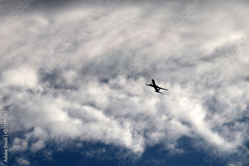 Airplane flying in the sky on background of clouds. Silhouette of a commercial plane during the turn