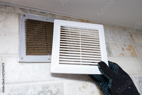 repair service man removing a dirty air filter on a house so he can replace it with a new clean. Extremely dirty and dusty white plastic ventilation air grille at home close up, harmful for health  photo