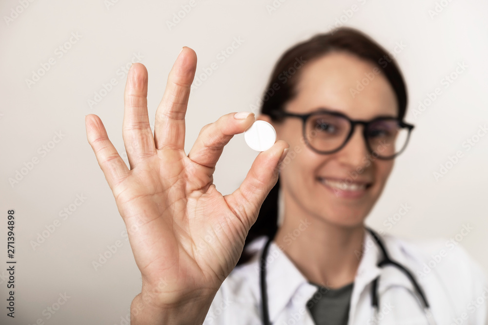 Young female doctor holds a round white pill in her hand Young female doctor holds a round white pill in her hand