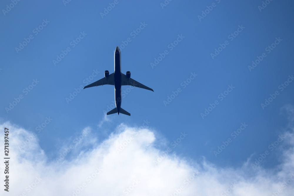 Airplane in the blue sky with white clouds. Commercial plane in a flight close up, bottom view Airplane in the blue sky with white clouds. Commercial plane in a flight close up, bottom view