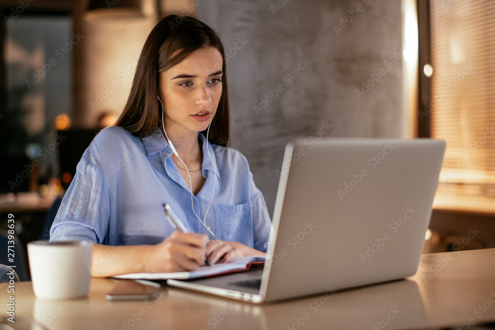 Young woman with headphones using laptop, taking notes Young woman with headphones using laptop, taking notes