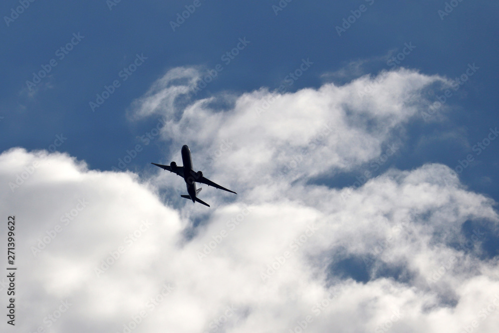Airplane flying up in a blue sky on background of white clouds. Silhouette of a commercial plane during the taking off