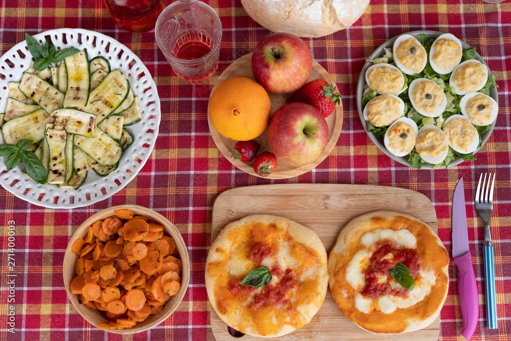 Red checkered tablecloth in the table outdoor in the terrace. Wooden cutting board with pizza. Vegetables and eggs. Fresh natural fruits Red checkered tablecloth in the table outdoor in the terrace. Wooden cutting board with pizza. Vegetables and eggs. Fresh natural fruits