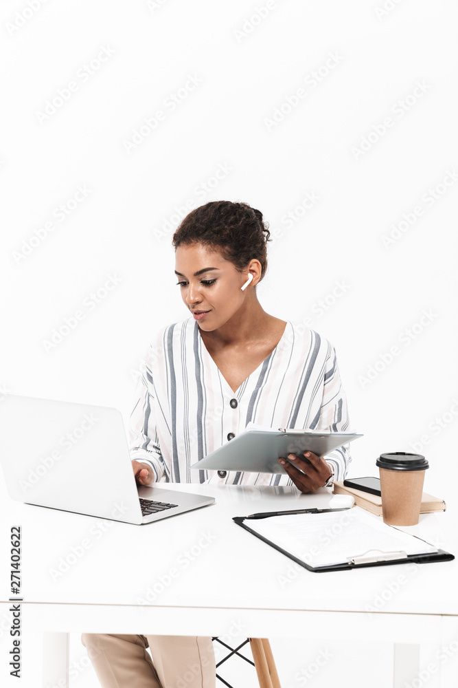 Beautiful african woman posing isolated over white wall background using laptop computer talking with earphones holding clipboard. Beautiful african woman posing isolated over white wall background using laptop computer talking with earphones holding clipboard.