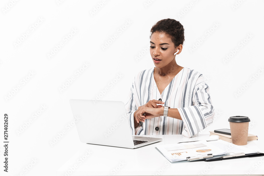 African woman posing isolated over white wall background using laptop computer listening music with earphones use watch clock. African woman posing isolated over white wall background using laptop computer listening music with earphones use watch clock.