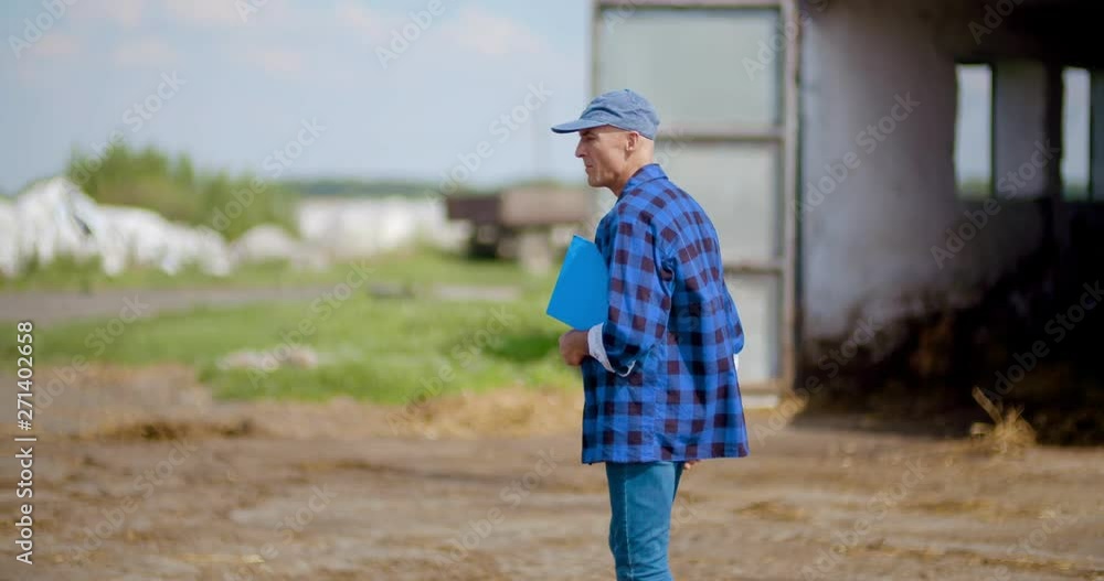 Farmer gesturing while writing on clipboard against barn Farmer gesturing while writing on clipboard against barn